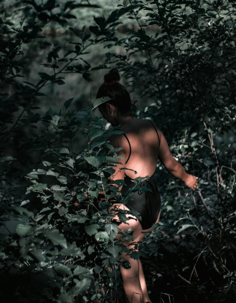 Woman walking into a dark forest wearing a black swim suit